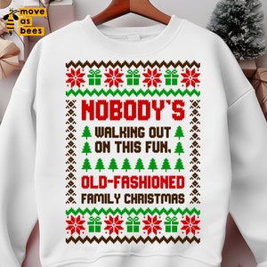 May include: White sweatshirt with a Christmas-themed design. The design features red and green gift boxes, snowflakes, and Christmas trees. The text reads "NOBODY'S WALKING OUT ON THIS FUN. OLD-FASHIONED FAMILY CHRISTMAS."