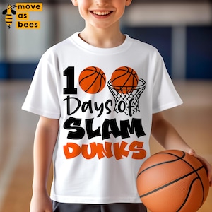 May include: White t-shirt with the text "100 Days of Slam Dunks" and basketball graphics. A child is wearing the shirt and holding a basketball. The shirt has a basketball and net graphic.