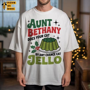 May include: White t-shirt with a Christmas-themed graphic. The design features the text "Aunt Bethany Does Your Cat By Any Chance Eat Jello" in green and red, along with a green Jello mold illustration and holly accents.