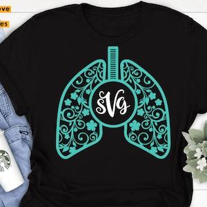 Op de afbeelding: Zwart T-shirt met een turquoiseblauw ontwerp van een gestileerde long met bloemmotieven. De long heeft een cirkel in het midden met de tekst "SVG" in wit.