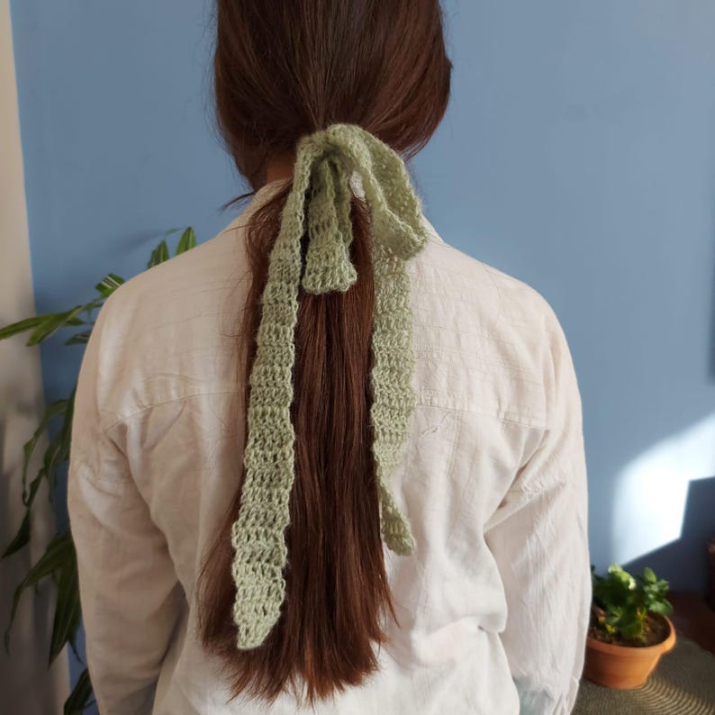 May include: A green crocheted hair tie tied in a bow around a ponytail.