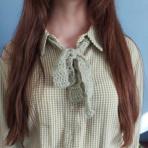 May include: A green gingham shirt with a crocheted green bow tied at the collar.