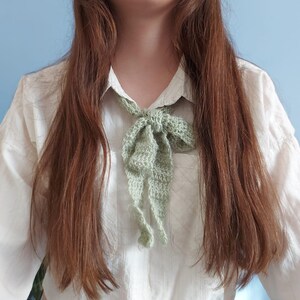 May include: A person wearing a white shirt with a green crocheted bow tie around the neck.