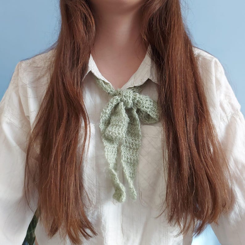 May include: A person wearing a white shirt with a green crocheted bow tie around the neck.