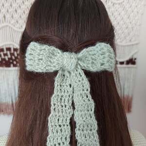 May include: A light green crocheted bow with a lacy design, tied in a person's hair.
