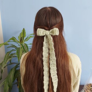 May include: A light green crocheted bow hair clip with long tails. The bow is tied in a simple knot and the tails are long and flowing.