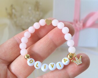 Pulseira personalizada para bebê em quartzo rosa, com pingente de coração e coroa em ouro 18K, ideal para batizado ou chá de bebê com o nome de uma princesa.