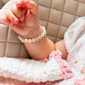 Puede incluir: Una pulsera de cuentas con esferas blancas y cuentas redondas blancas con letras doradas que forman la palabra MAGNOLIA. La pulsera est&aacute; compuesta por una alternancia de cuentas tipo perla y cuentas con letras en forma circular.