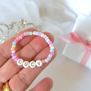 May include: A colorful beaded bracelet with the name "LUCY" spelled out in white letters with gold lettering. The bracelet is on a hand.