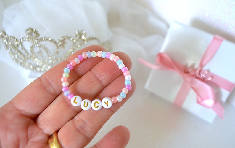 May include: A colorful beaded bracelet with the name "LUCY" spelled out in white letters with gold lettering. The bracelet is on a hand.