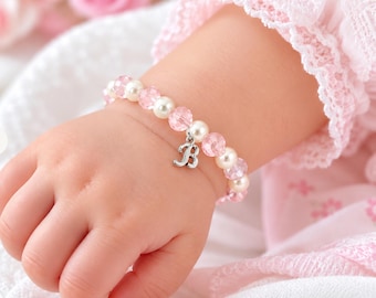 May include: A beaded bracelet featuring alternating light pink faceted beads and smooth white pearls. The bracelet includes a silver-toned metal charm in the shape of the letter B, which hangs from the center of the circular beaded strand.