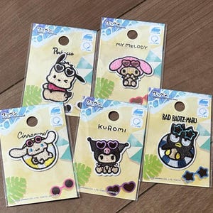 May include: Five Sanrio character embroidered patches on individual display cards. Characters include Pochacco, My Melody, Cinnamoroll, Kuromi, and Bad Badtz-Maru. Each patch features a character wearing heart-shaped sunglasses. The cards display the character names and include icons for iron-on and adhesive application.