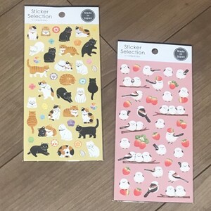 May include: Two sticker sheets. One has cat illustrations in various poses on a yellow background. The other has bird and strawberry illustrations on a pink background. Both sheets have the text "Sticker Selection" and "Made in Japan".