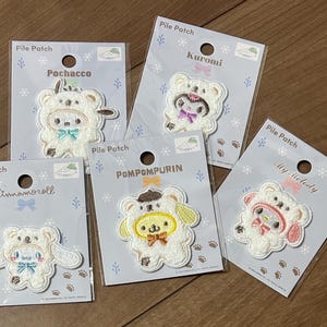 May include: Five Sanrio character pile patches on individual display cards. Each patch features a character wearing a white bear hood. The characters include Pochacco, Kuromi, Cinnamoroll, Pompompurin, and My Melody, each with distinct colored accents and bows.
