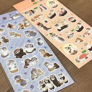 May include: Two sheets of stickers featuring adorable cartoon cats dressed in various costumes, including a panda, a red panda, and a lion. The stickers are on a blue and orange background with stars and flowers.