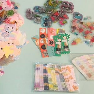 May include: Assortment of colorful stickers featuring various cartoon animals, including cats, penguins, and bears. The stickers are arranged in three groups on a light blue surface.