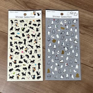 May include: Two sheets of Sticker Selection stickers made in Japan. The left sheet features black cats and witches on a cream background. The right sheet displays white and gold ghost figures on a gray background, including various poses and items.