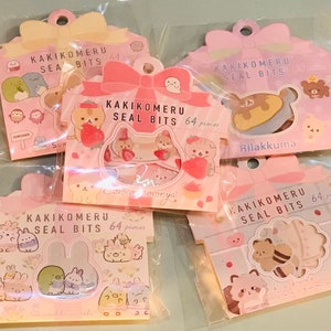 May include: Four pink and white packages of decorative stickers with the text "Kakikomeru Seal Bits 64 pieces" on each package. The stickers feature various cartoon characters, including a bear, a rabbit, and a cat.