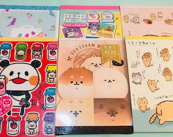 May include: Four different memo pads featuring cute cartoon animal illustrations. The memo pads are pink, yellow, and blue with white borders. The illustrations include a panda bear, a dog, and a cat. The text on the memo pads reads "Ichigo", "Yeastken", "Chigiri Memo", and "Korokoro Koronya".