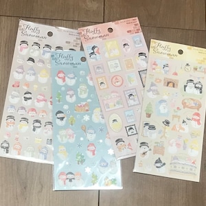 May include: Four sticker sheets featuring various snowman designs. Each sheet has the words "Fluffy Snowman" at the top. The stickers depict snowmen with hats, scarves, and other winter accessories. The backgrounds are light pink, light blue, and beige.