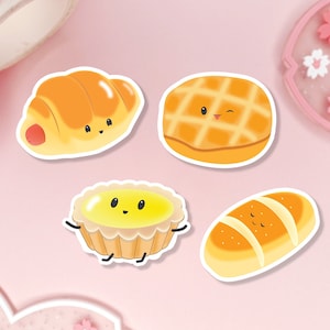 Peut inclure: Cinq articles de boulangerie dessinés avec des visages heureux. Un croissant, un pain avec un motif en grille, une tarte avec une garniture jaune et deux pains.