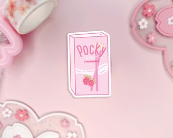 Puede incluir: Una pegatina rosa y blanca con una caja de galletas Pocky de fresa. La caja tiene un fondo rosa con texto blanco que dice "Pocky Glico Strawberry". Hay tres palitos Pocky rosas y blancos dentro de la caja.