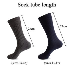 K&ouml;nnte beinhalten: Zwei gerippte Socken, eine anthrazitfarbene und eine marineblaue, mit dem Text Sock tube length. Die graue Socke misst 23 cm f&uuml;r die Gr&ouml;&szlig;en 39-43, die marineblaue Socke misst 27 cm f&uuml;r die Gr&ouml;&szlig;en 43-47, dargestellt mit Messlinien.