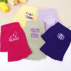 以下が含まれることがあります： ピンク、イエロー、ラベンダー、グリーン、ネイビーブルーなど、さまざまな色の指なし手袋の詰め合わせ。各手袋には、「Yoga Time」、「Pilates Studio」、蓮の花など、刺繍されたテキストまたはデザインが施されています。手袋は柔らかいニット素材で作られています。