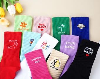 Puede incluir: Una colección de calcetines de canalé coloridos con varios diseños y textos bordados. Los calcetines son en tonos de rojo, verde, azul, rosa, blanco y morado. Algunos calcetines presentan diseños florales, un perro, un cóctel y las palabras "BEST MAMA", "Bride", "YOUR NAME" y "BEST BABA".