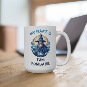 May include: White ceramic mug with a blue and white illustration of a wizard with a long white beard and a pointed hat. The text "My name is Tom Bombadil" is printed on the mug.