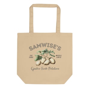 Op de afbeelding: Een beige canvas draagtas met de tekst "Samwise's" in een grijze cirkel. De tekst "The Shire" en "Middle Earth" staan aan weerszijden van de cirkel. Onder de cirkel staat een tekening van een aardappelplant met aardappelen. De tekst "Garden Fresh Potatoes" staat onder de tekening.