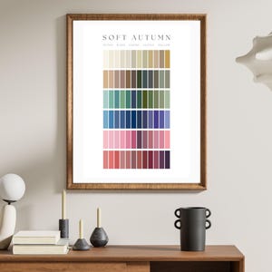 May include: A framed print titled "Soft Autumn" displays a color palette with rows of various shades. The palette includes beige, brown, green, blue, and pink hues. The frame is a warm brown, and the print is displayed on a wooden surface.