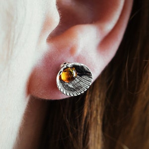 May include: A close-up of a person's ear with a silver earring featuring a small amber stone.