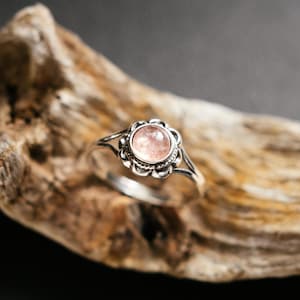 Op de afbeelding: Een zilveren ring met een delicaat bloemmotief en een roze edelsteen in het midden.