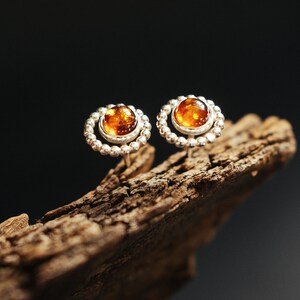 May include: A pair of silver earrings with amber stones set in a circle of small beads.