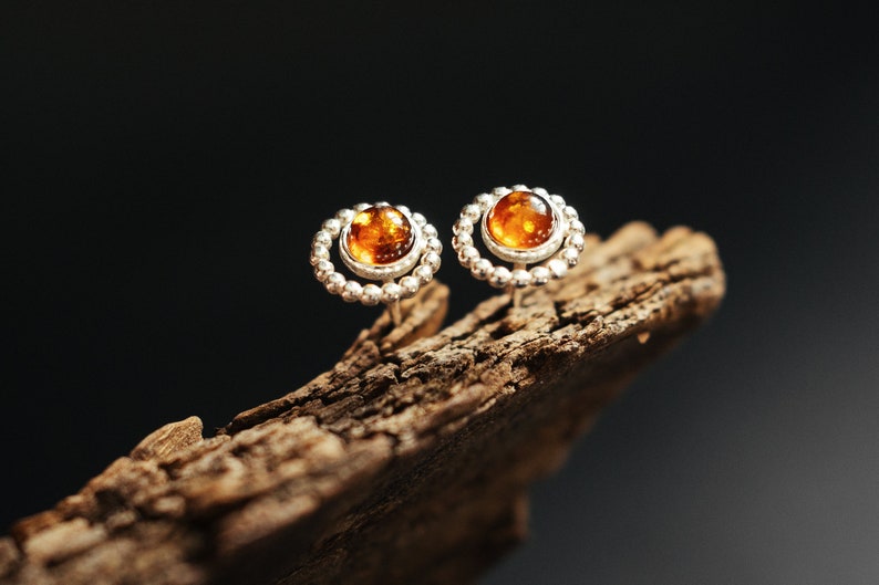 May include: A pair of silver earrings with amber stones set in a circle of small beads.