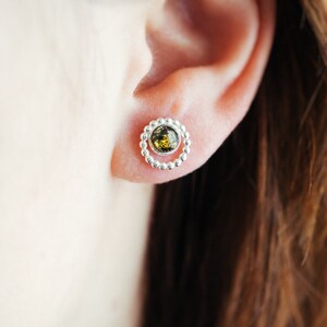 May include: A pair of silver earrings with a small green gemstone in the centre of each earring. The earrings are in the shape of a circle with a beaded border.