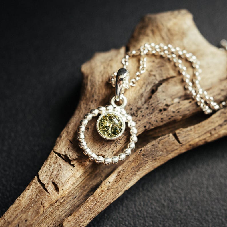 Close-up of a delicate round pendant made of 925 sterling silver with a circle of tiny silver beads and a central green Baltic amber cabochon, minimalist design, diameter 15 mm