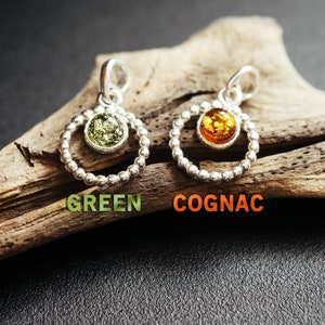 Close-up of a delicate round pendant made of 925 sterling silver with a circle of tiny silver beads and a central green Baltic amber cabochon, minimalist design, diameter 15 mm