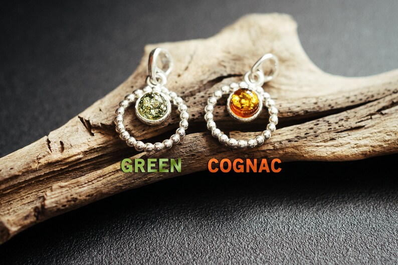 Close-up of a delicate round pendant made of 925 sterling silver with a circle of tiny silver beads and a central green Baltic amber cabochon, minimalist design, diameter 15 mm