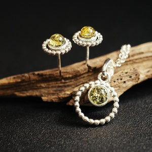 Close-up of a delicate round pendant made of 925 sterling silver with a circle of tiny silver beads and a central green Baltic amber cabochon, minimalist design, diameter 15 mm