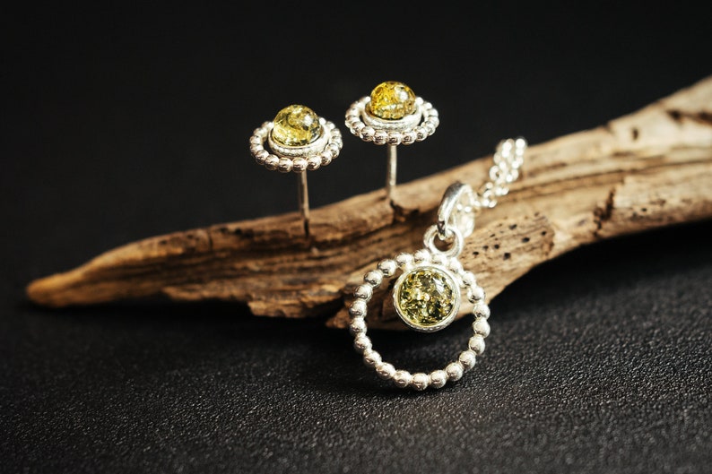 Close-up of a delicate round pendant made of 925 sterling silver with a circle of tiny silver beads and a central green Baltic amber cabochon, minimalist design, diameter 15 mm
