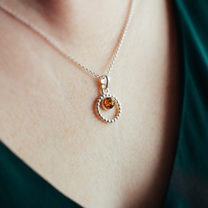 May include: A silver necklace with a round pendant featuring a small amber stone.
