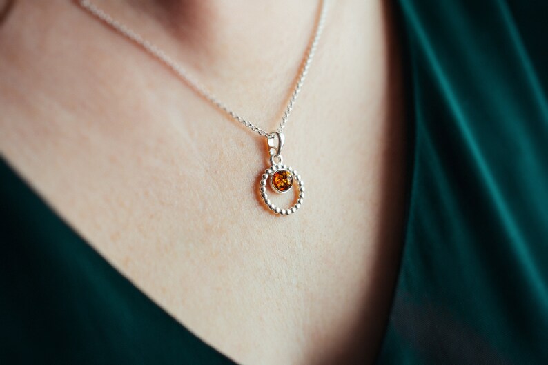 May include: A silver necklace with a round pendant featuring a small amber stone.