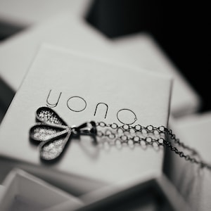 May include: A silver necklace with a delicate, three-leaf pendant, resting in a white box with the word "yono" printed on the lid.