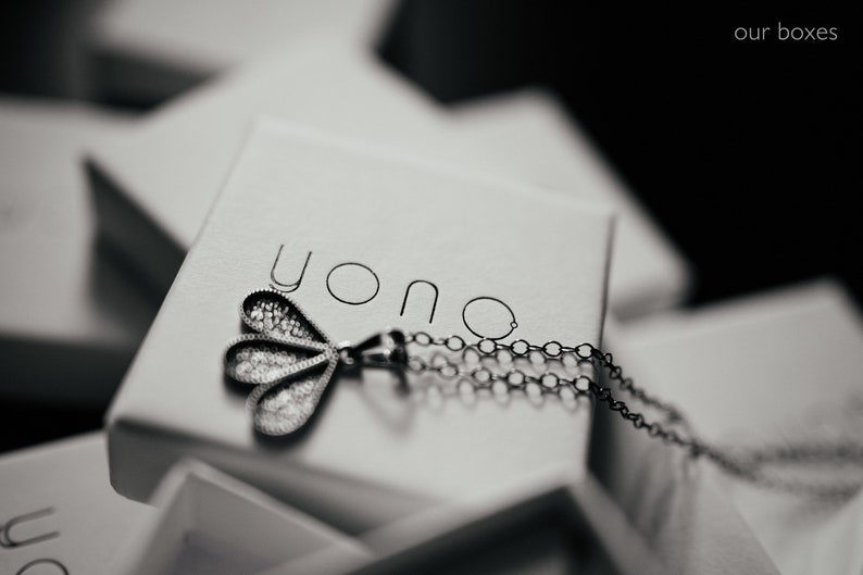 May include: A silver necklace with a delicate, three-leaf pendant, resting in a white box with the word "yono" printed on the lid.
