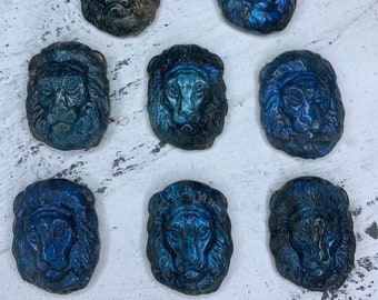 May include: Eight blue and green labradorite lion head carvings. The carvings are polished and have a iridescent sheen.