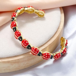 Pode incluir: Pulseira dourada com detalhes vermelhos, pretos e dourados. A pulseira é adornada com contas vermelhas, pontilhadas e ovais, conectadas por segmentos pretos. O design de punho aberto adiciona um toque moderno a esta joia.