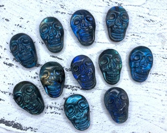 Puede incluir: Una colección de 10 tallas de cráneos de labradorita azul y negra. Los cráneos están todos tallados en un estilo similar, con una cara detallada y un acabado liso y pulido.