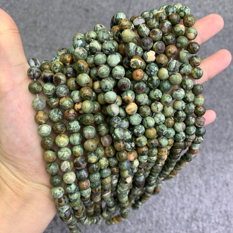 K&ouml;nnte beinhalten: Eine Str&auml;hne runder Edelsteinkugeln in Gr&uuml;n, Braun und Wei&szlig;. Die Perlen haben einen Durchmesser von etwa 6 mm und ein geflecktes, marmoriertes Aussehen.